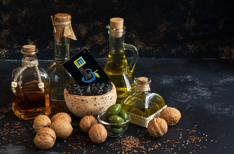 Verschiedene Öle aus Walnuss, Olive, Leinsamen und Sonnenblumenkernen vor grauem Hintergrund mit EDEKA-Nils-Meyer Karte