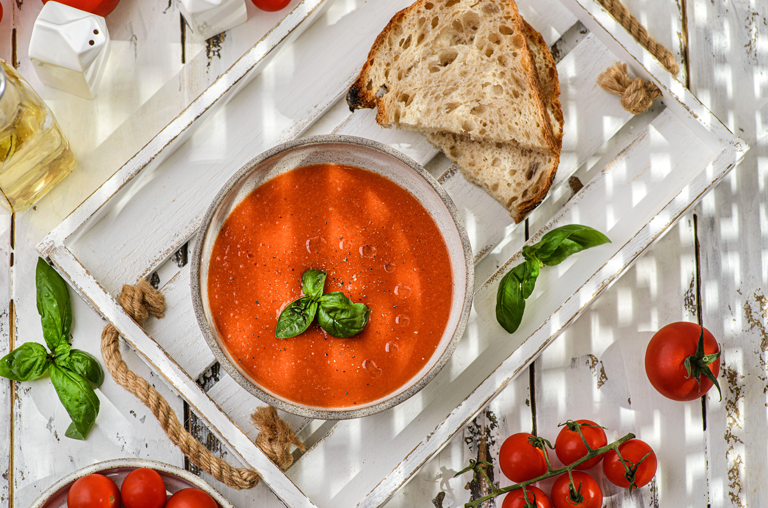 Bild einer Gazpacho auf Holztisch mit Brot im Schatten
