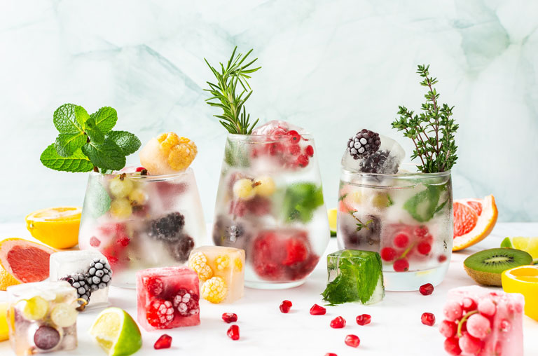 Cocktails mit gefüllten Eiswürfeln, in denen Beeren und Kräuter sind